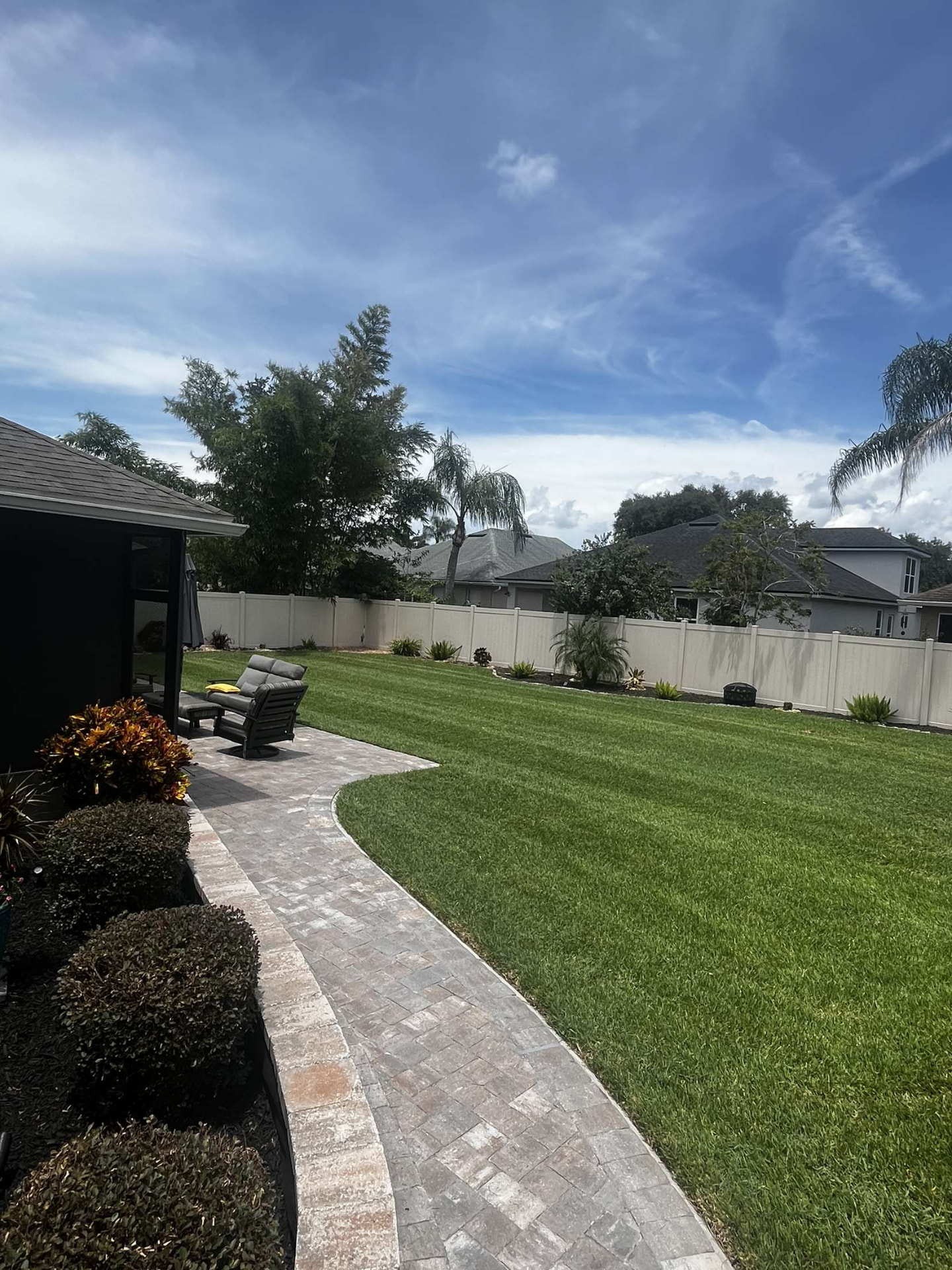Backyard with striped St. Augustine lawn, paver walkway and tropical beds